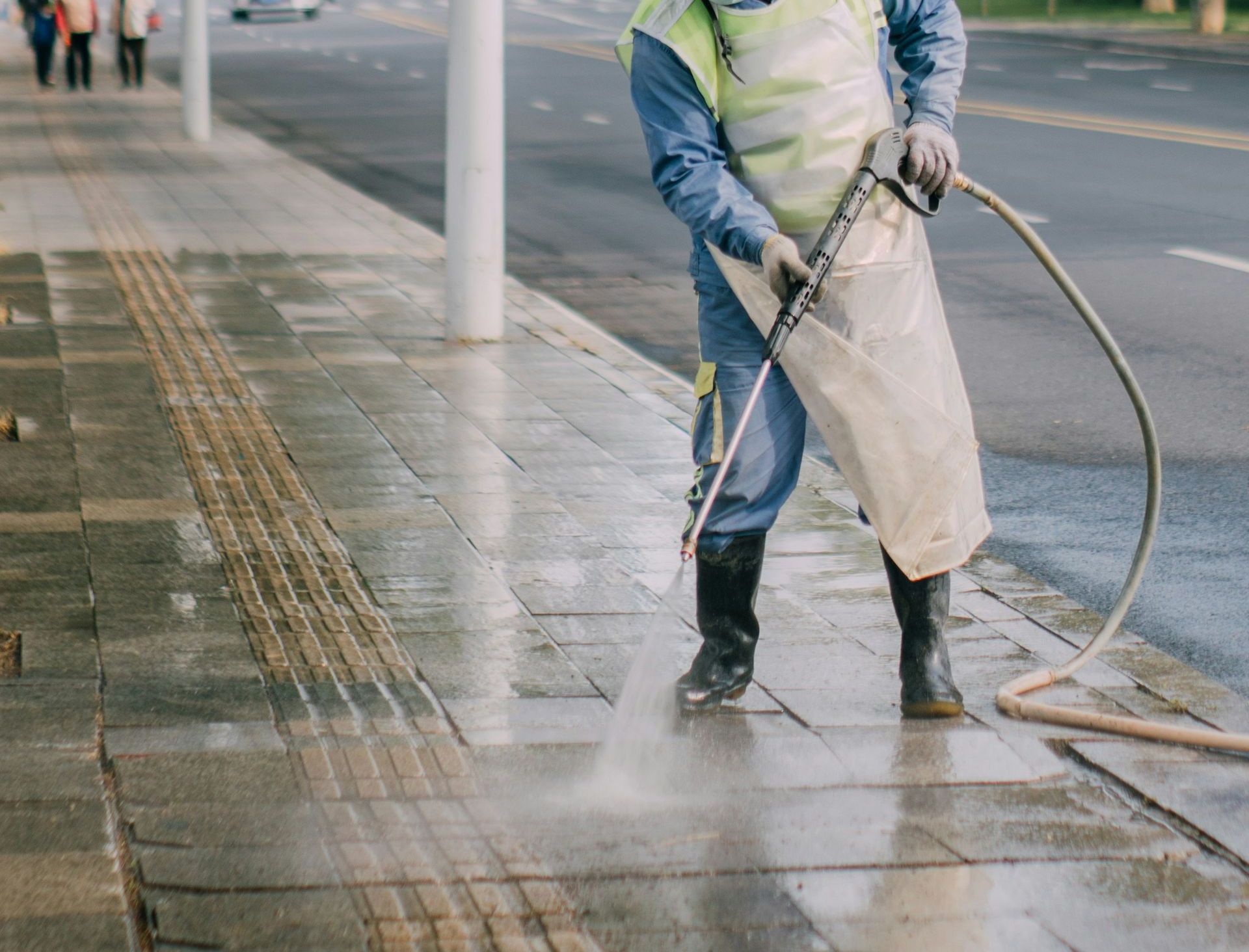 a man in a yellow vest is spraying water on a sidewalk