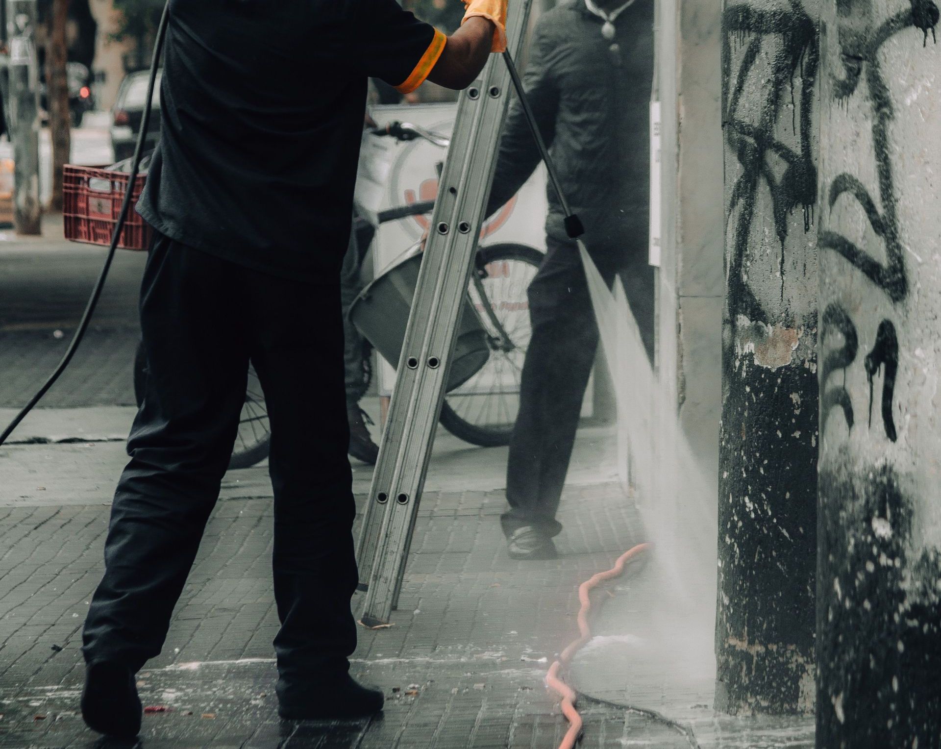 Workers cleaning graffiti off city building facade with a pressure hose.