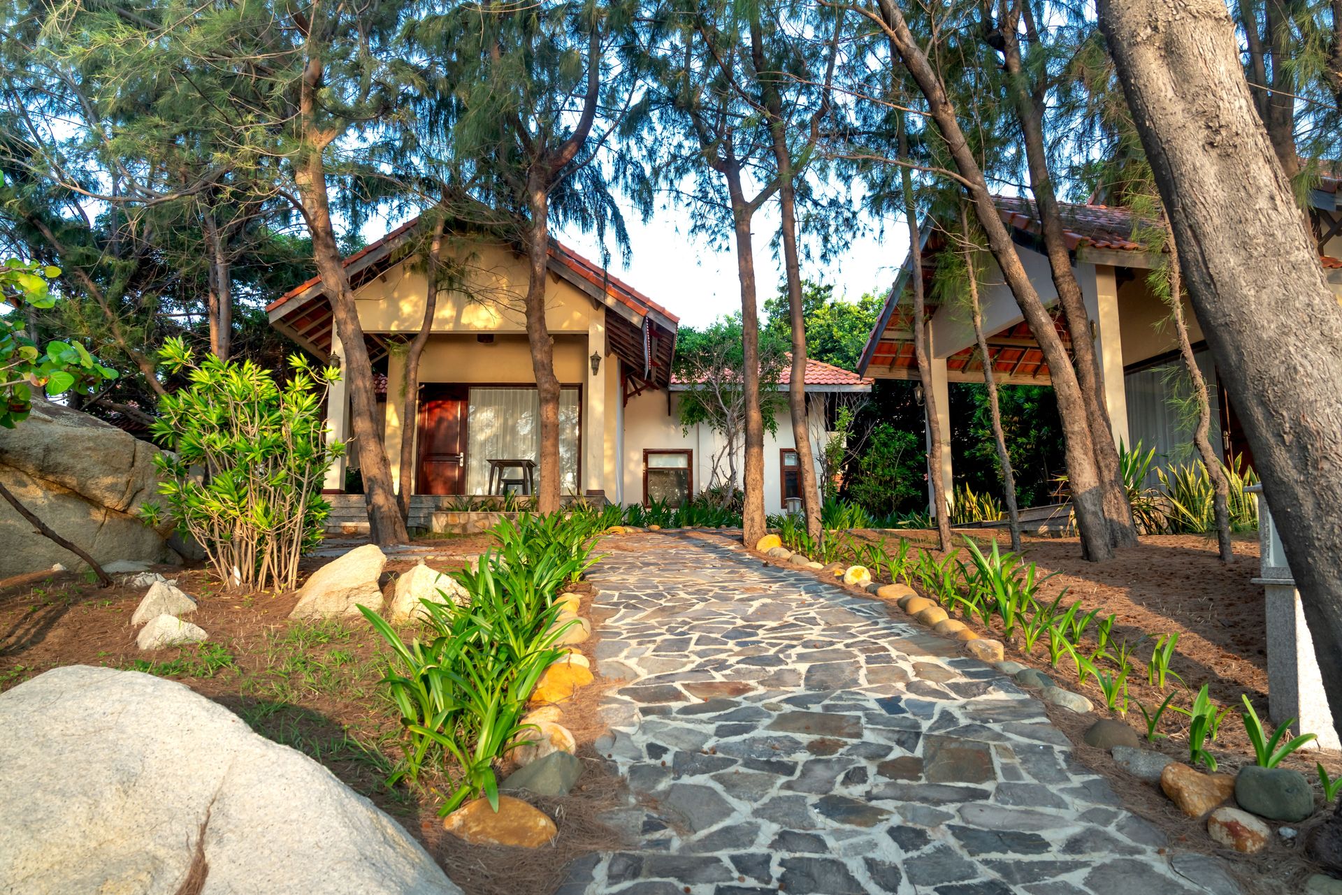 Explore tranquil summer houses surrounded by lush trees and stone walkways, exuding serene charm.