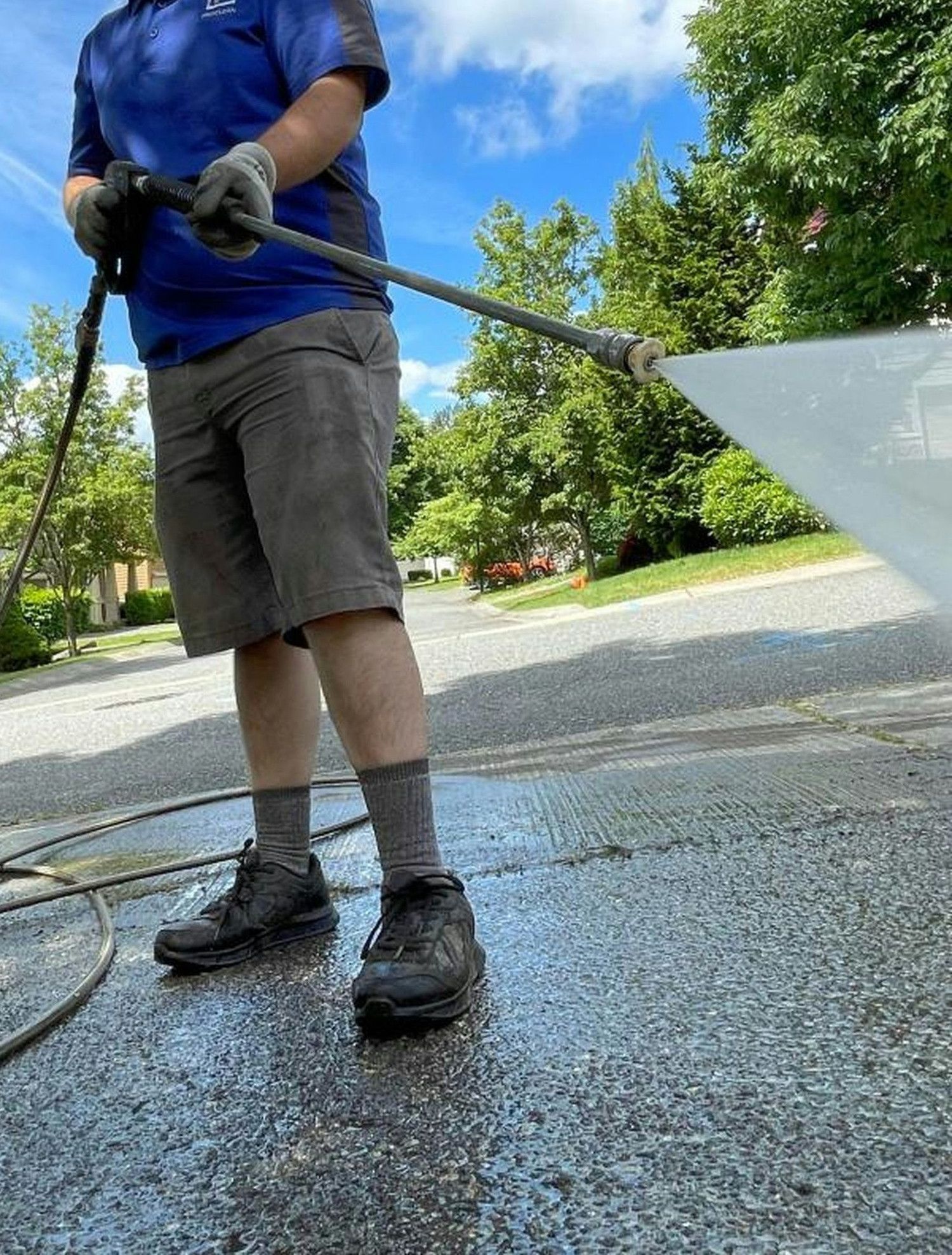 a man in a blue shirt is washing a driveway